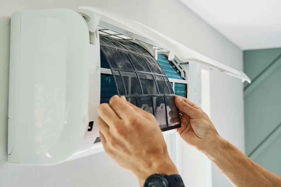 Technicien qui retire le filtre encrassé d’une climatisation murale pour l’entretien