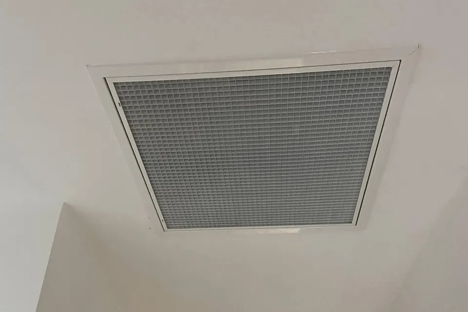 Grille de reprise blanche d’une climatisation gainable intégrée à un plafond blanc