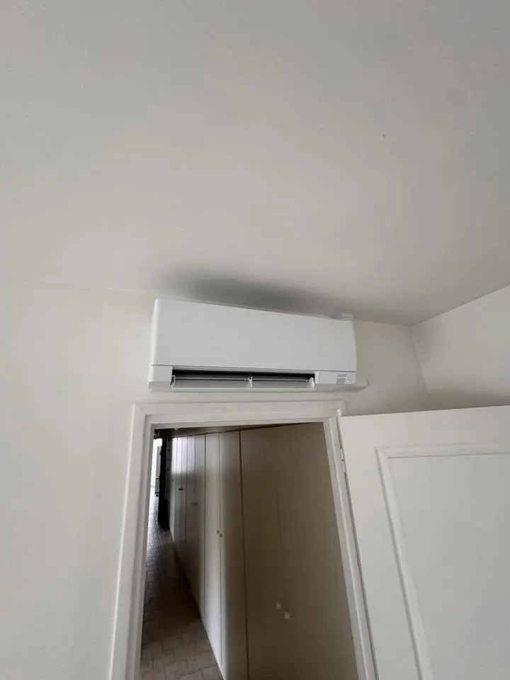 Climatiseur mural blanc Mitsubishi Electric installé au-dessus d’un encadrement de porte