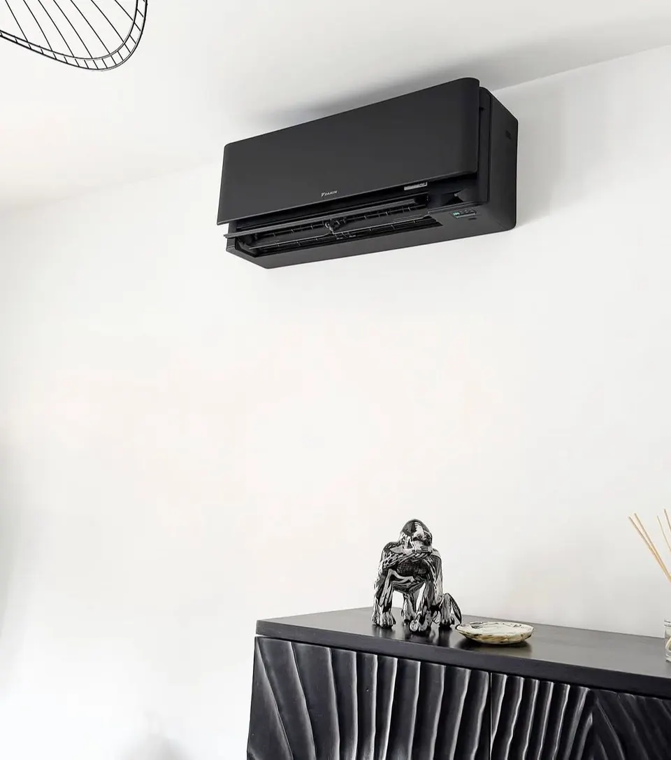 Climatiseur mural Daikin noir au-dessus d’un buffet noir dans un salon blanc