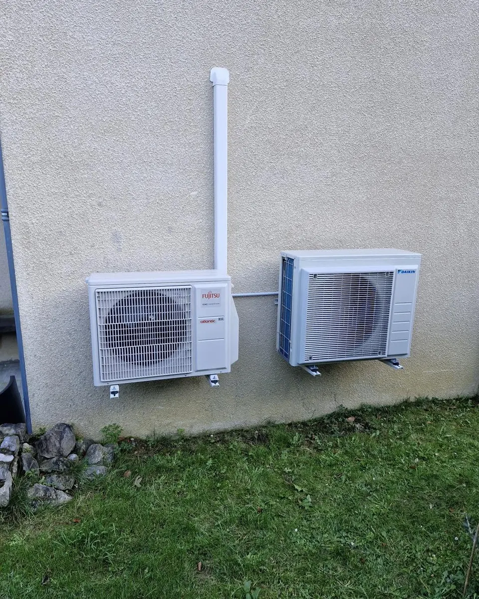 Deux groupes extérieurs de climatisation fixés sur une façade crépie, au-dessus d’une pelouse