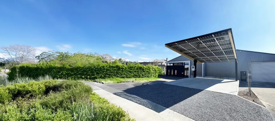 Grande ombrière couverte de panneaux solaires devant un bâtiment professionnel, avec borne de recharge