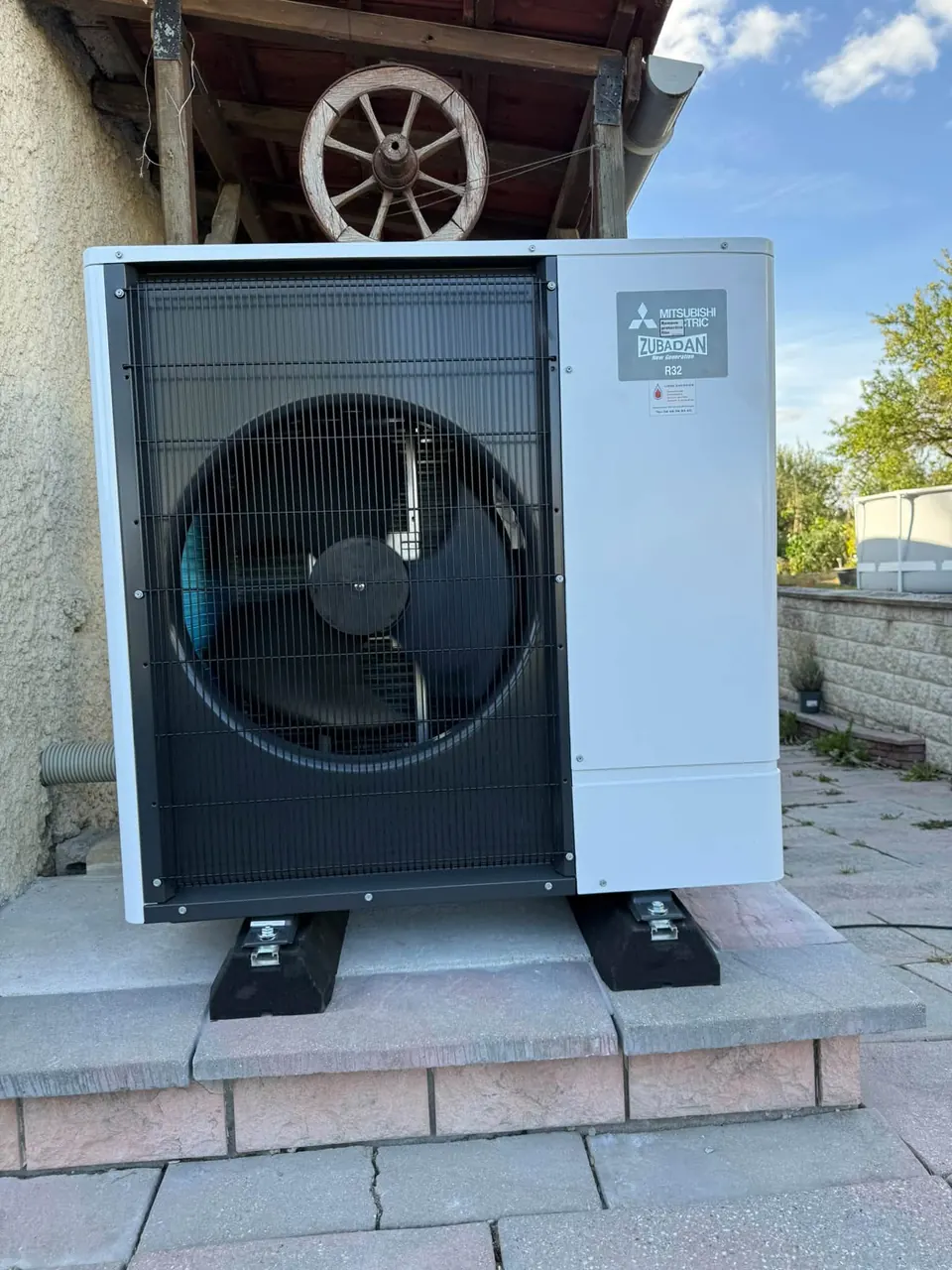 Groupe extérieur de pompe à chaleur Mitsubishi Electric Zubadan posé sur des plots, sous un auvent